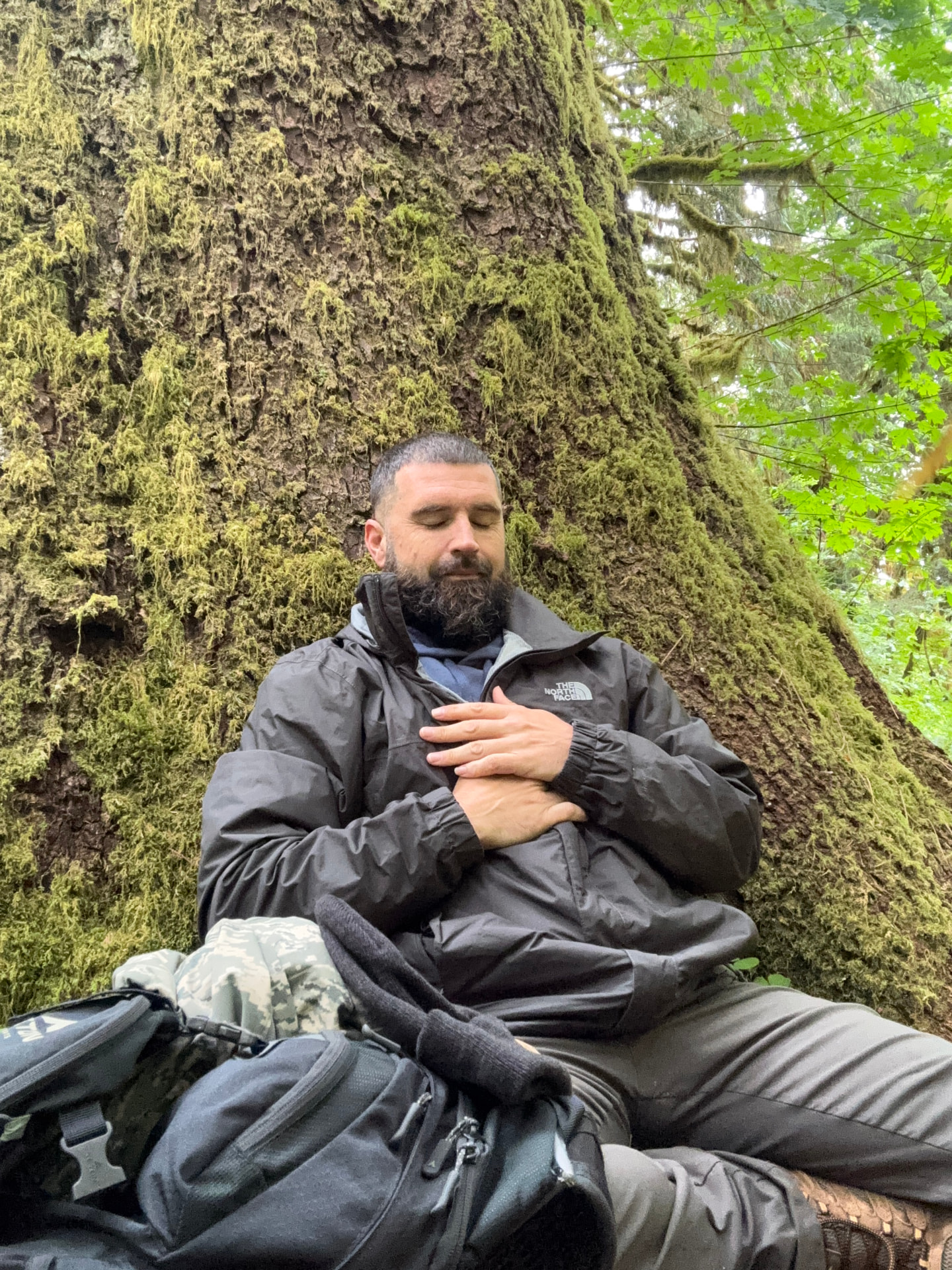 Antone Baillie meditating beside a moss-covered tree