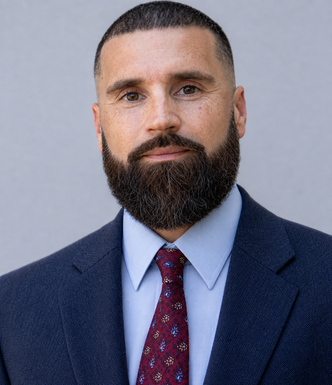 Formal professional portrait of Antone Baillie in a navy suit and patterned tie