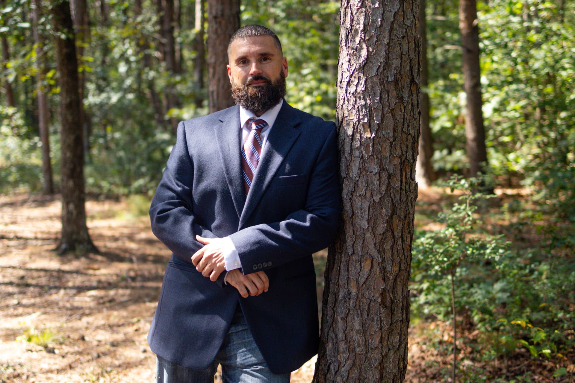 Portrait of Antone Baillie leaning against a pine tree in a sunlit forest